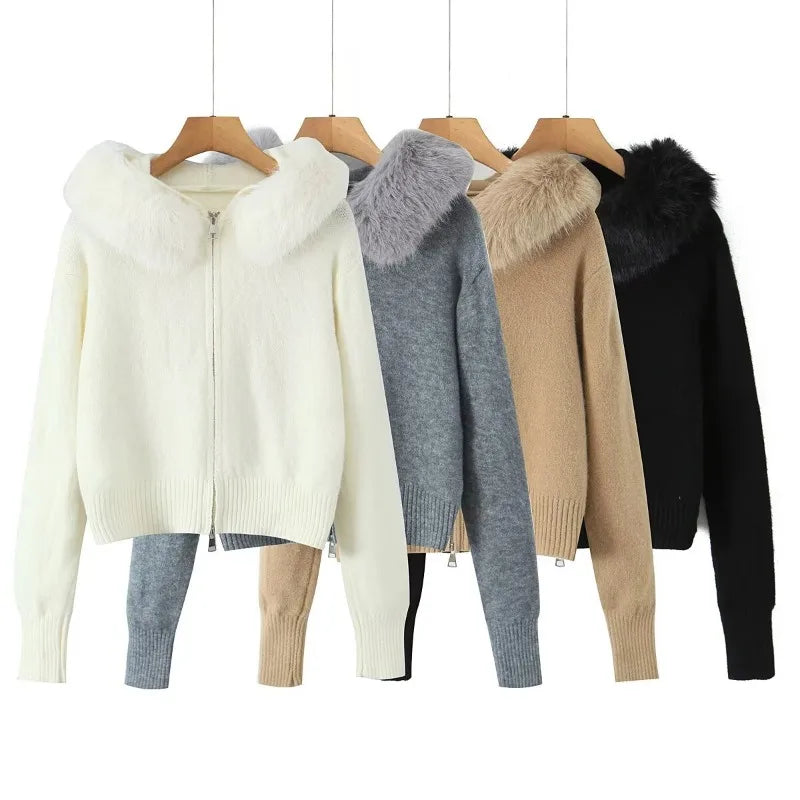 Four women's knit zip-front hooded sweaters with faux-fur or faux-fur-trimmed hoods, displayed on wooden hangers against a white background. The colors shown are off-white, heather gray, tan, and black.